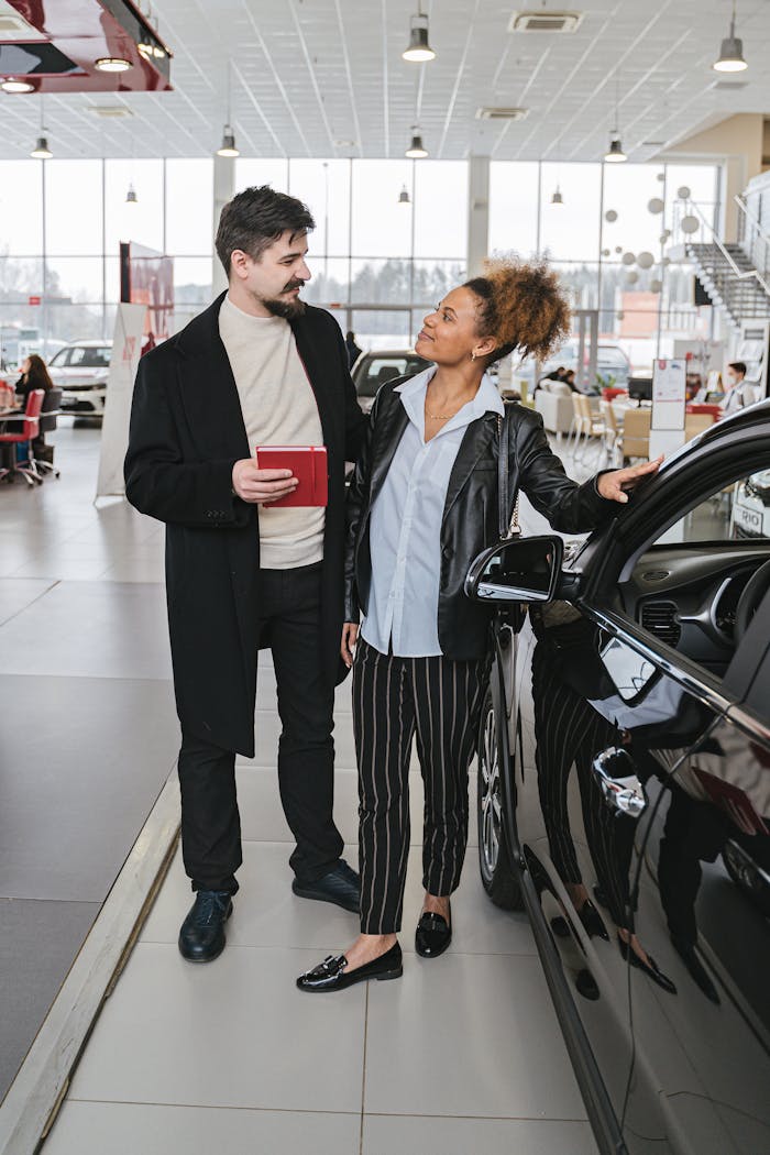 A man and woman examine a car in a dealership showroom, discussing possibilities.